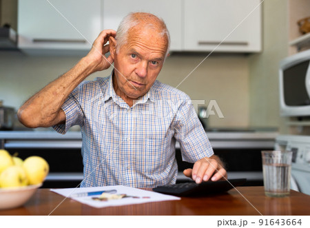 Man sitting at table at home calculating domestic finances and bills Man sitting at table at home calculating domestic finances and bills 91643664