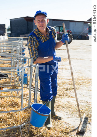 Smiling farmer standing near outdoors stall with calves Smiling farmer standing near outdoors stall with calves 91644135