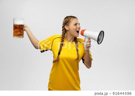 Young excited woman in yellow football kit holding beer mug and supports favorite team. Soccer fans, competition, sport, oktoberfest concept Young excited woman in yellow football kit holding beer mug and supports favorite team. Soccer fans, competition, sport, oktoberfest concept 91644396