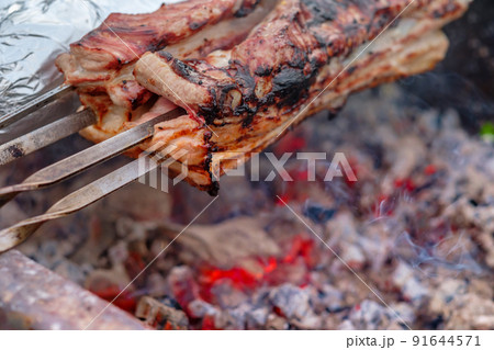 Juicy slices of pork meat are strung on skewers and grilled in charcoal grill. 91644571