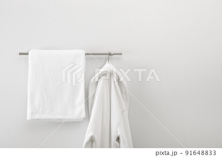 Rack with clean bathrobe and towel on light wall 91648833