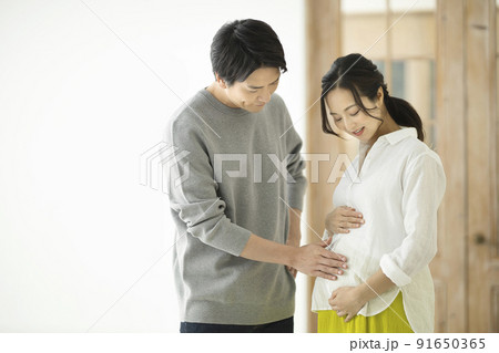 妊婦のおなかに手を添えて話すカップル 91650365