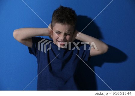 Scared little boy closing his ears near blue wall. Domestic violence concept Scared little boy closing his ears near blue wall. Domestic violence concept 91651544