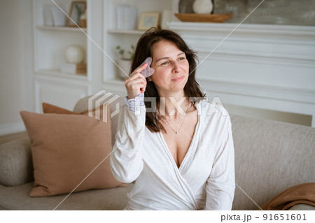 Shot of woman holding pink gouache scraper to massage her face during her 91651601