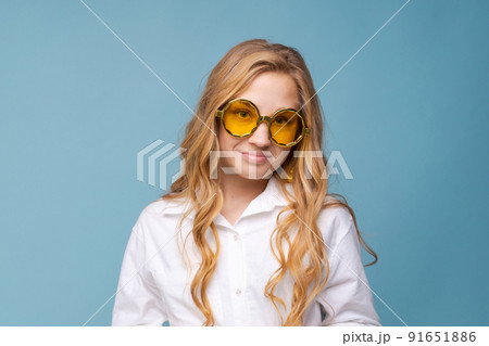 Cheerful young woman wearing yellow glasses smiling at camera against blue 91651886