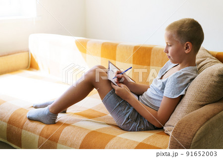 Boy sitting on couch at home doing homework for school. Caucasian school-age Boy sitting on couch at home doing homework for school. Caucasian school-age 91652003
