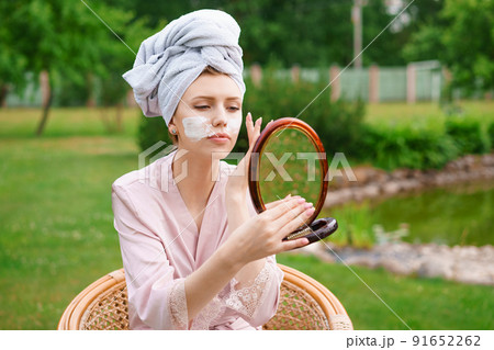 Beautiful young woman applying moisturizer on her face after shower while Beautiful young woman applying moisturizer on her face after shower while 91652262