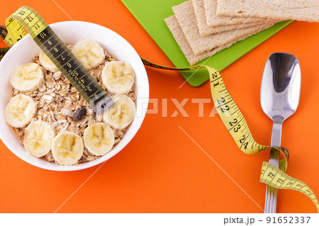 oatmeal and crispbread lie with spoon and measuring tape on orange background oatmeal and crispbread lie with spoon and measuring tape on orange background 91652337