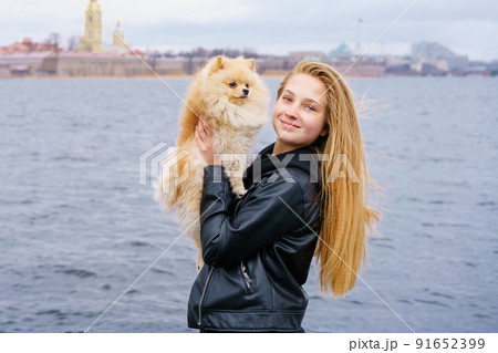 Young woman hugs spitz dog outdoors on embankment of city river in black 91652399