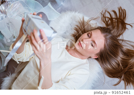 Cute woman lies on the floor with gift in her hand by the christmas tree. Happy Cute woman lies on the floor with gift in her hand by the christmas tree. Happy 91652461