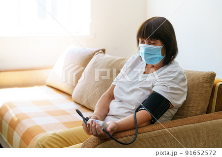 An elderly woman wearing mask measures her blood pressure with an electronic An elderly woman wearing mask measures her blood pressure with an electronic 91652572