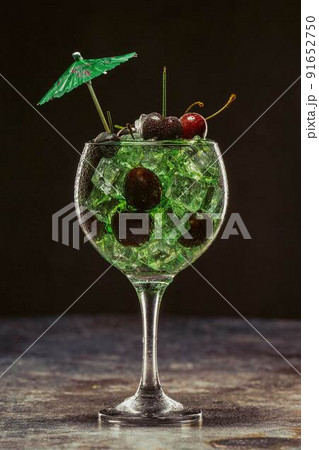 Green cocktail with ice and cherries in a glass decorated with umbrellas 91652750