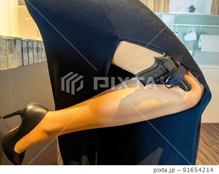 a woman in an evening black dress holds a pistol in stockings. black, small, compact pistol. military weapon. special agent on a mission 91654214