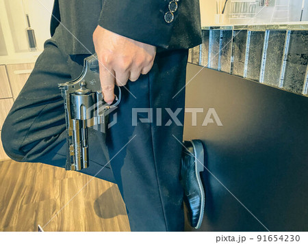 a man in a festive suit and smooth, patent-leather shoes holds a pistol. black, small, compact pistol. military weapon. special agent on a mission 91654230