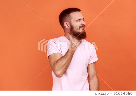 Inflamed throat. Portrait of bearded man touching painful neck, suffering sore throat, tonsillitis symptom, medical concept, wearing pink T-shirt. Indoor studio shot isolated on orange background. 91654660