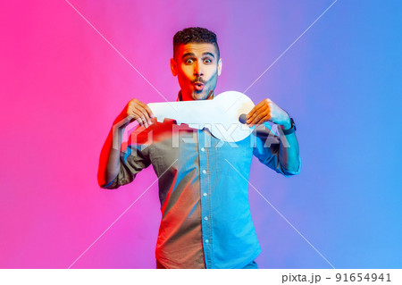 Portrait of astonished man in shirt holding huge paper key and being amazed to get new home, real estate purchase, rental service. Indoor studio shot isolated on colorful neon light background. 91654941
