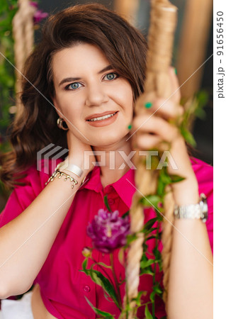 an attractive woman in a pink blouse with peonies on the swing. an attractive woman in a pink blouse with peonies on the swing. 91656450