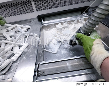 A man working with a working vacuum cleaner to clean the white powder of polyamide from a model printed on a 3D printer inside a 3D printer. Cleaning objects printed on an industrial powder 3D printer 91667316