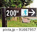 公園のランニングコースの標識と緑に囲まれたテニスコート 91667957