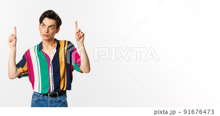 Attractive gay man looking thoughtful, pointing fingers up at logo, standing over white background 91676473