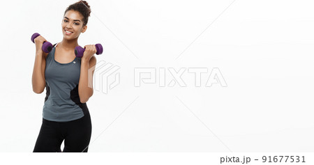 Healthy and Fitness concept - Beautiful American African lady in fitness clothes workout with dumbbell. Isolated on white background. Healthy and Fitness concept - Beautiful American African lady in fitness clothes workout with dumbbell. Isolated on white background. 91677531