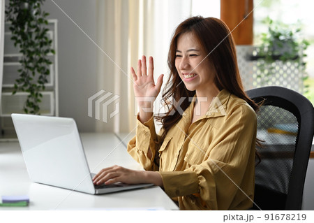 Cheerful young woman looking at her laptop screen, communicating by video conference on laptop computer 91678219