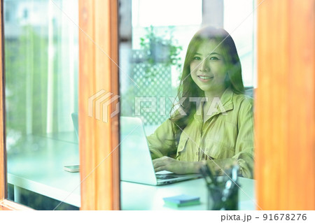 Through window view of positive businesswoman using laptop computer at home office Through window view of positive businesswoman using laptop computer at home office 91678276