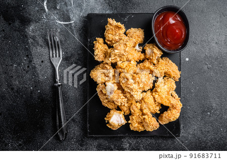 Crispy Fried breadcrumb covered chicken popcorn with ketchup. Black background. Top view Crispy Fried breadcrumb covered chicken popcorn with ketchup. Black background. Top view 91683711