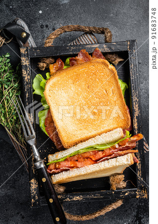 Homemade toasted BLT sandwich with bacon, tomato and lettuce in wooden tray. Black background. Top view 91683748