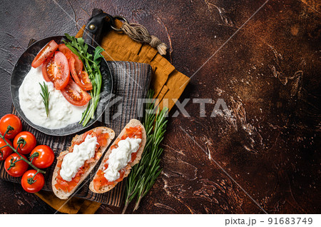 Bruschettas with stracciatella cheese, chopped cherry tomatoes and rosemary. Dark background. Top view. Copy space 91683749