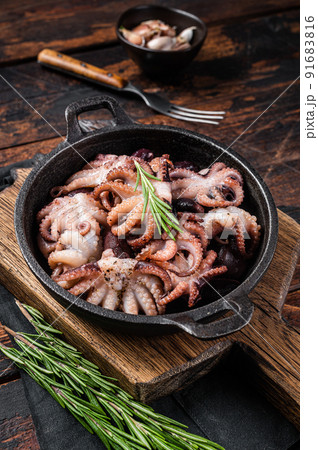 Fried baby octopuses in a skillet with herbs. Wooden background. Top view 91683816