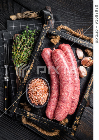 Raw sausages Bratwurst, fresh meat in wooden tray with thyme. Wooden background. Top view 91683920