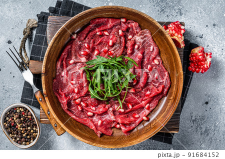 Classic beef meat carpaccio with arugula and pomegranate seeds. Gray background. Top view Classic beef meat carpaccio with arugula and pomegranate seeds. Gray background. Top view 91684152