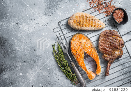 Set of bbq grilled meat steaks salmon, beef and turkey on a grill. Gray background. Top view. Copy space Set of bbq grilled meat steaks salmon, beef and turkey on a grill. Gray background. Top view. Copy space 91684220