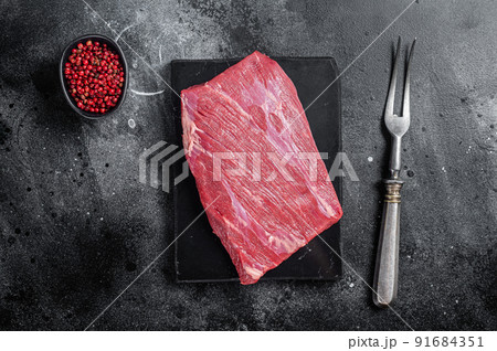 Prime choice flank steak, raw beef meat on marble board with herbs. Black background. Top view 91684351