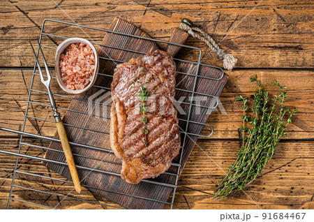 Grilled striploin or New York beef meat steak cooked on BBQ. Wooden background. Top view Grilled striploin or New York beef meat steak cooked on BBQ. Wooden background. Top view 91684467