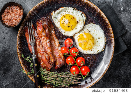 Breakfast with fried eggs and bacon with herbs in plate. Black background. Top view 91684468