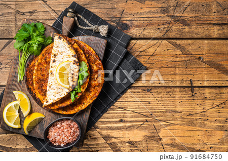 Turkish cuisine made with thin dough and minced beef meat lahmacun on wooden board with herbs. Wooden background. Top view. Copy space 91684750