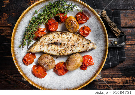 Grilled halibut fish steaks with tomato and potato in plate. Wooden background. Top view 91684751