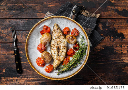 Grilled halibut fish steaks with tomato and potato in plate. Wooden background. Top view 91685173