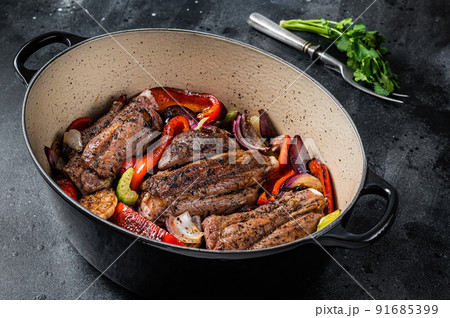 Braised slow cooked lamb shank in red wine sauce with vegetables in cooking pot. Black background. Top view Braised slow cooked lamb shank in red wine sauce with vegetables in cooking pot. Black background. Top view 91685399