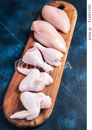 Chicken meat assortment. Raw parts - drumstick, breast fillet, wings, thigh. Blue background. Top view Chicken meat assortment. Raw parts - drumstick, breast fillet, wings, thigh. Blue background. Top view 91685400