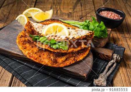 Turkish cuisine made with thin dough and minced beef meat lahmacun on wooden board with herbs. Wooden background. Top view 91685553