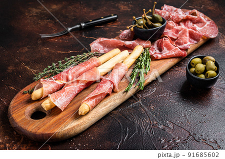 Meat appetizer platter with grissini sticks, Prosciutto crudo, Salami and Coppa Sausage and olives. Dark background. Top view Meat appetizer platter with grissini sticks, Prosciutto crudo, Salami and Coppa Sausage and olives. Dark background. Top view 91685602