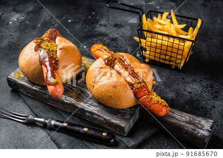 Deutsche Bockwurst sausage in a bun with French fries and curry sauce, currywurst. Black background. Top view Deutsche Bockwurst sausage in a bun with French fries and curry sauce, currywurst. Black background. Top view 91685670