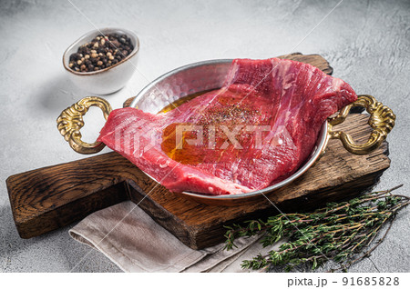 Flap or flank steak, raw beef meat in skillet with herbs and olive oil. White background. Top view 91685828