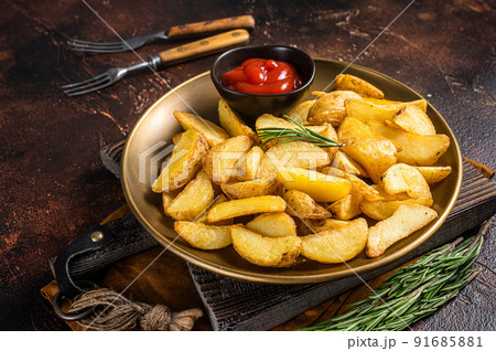 Seasoned potato wedges with rosemary and tomato sauce in a plate. Dark background. Top view 91685881
