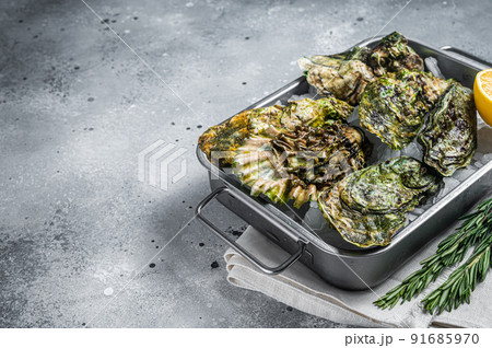 Fresh closed oysters, raw seafood with lemon and ice in steel tray. Gray background. Top view. Copy space 91685970