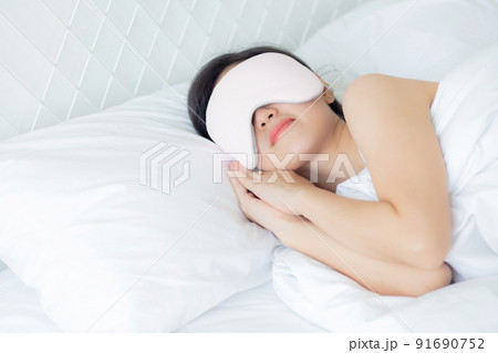 Beautiful young asian woman wearing cover eye and sleeping on bed with head on pillow comfort. 91690752