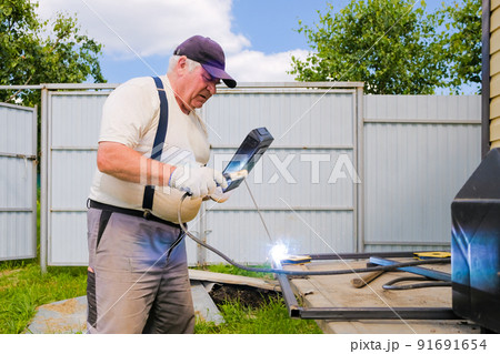 Senior gray-haired man performs welding work on metal 91691654